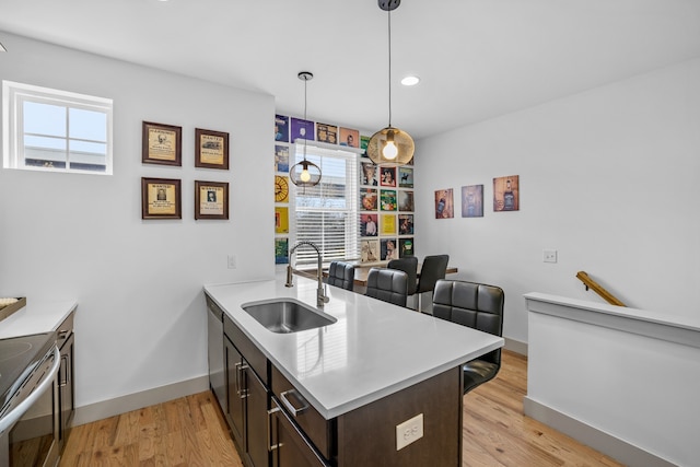 kitchen featuring kitchen peninsula, sink, dark brown cabinetry, decorative light fixtures, and light hardwood / wood-style floors