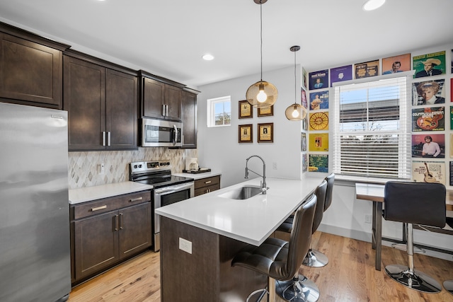 kitchen featuring sink, a breakfast bar area, hanging light fixtures, stainless steel appliances, and light hardwood / wood-style flooring