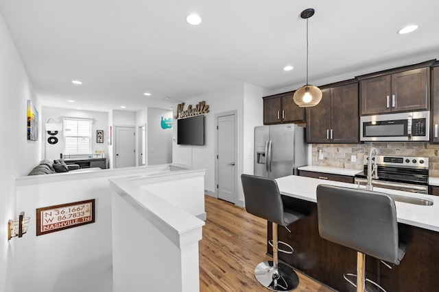 kitchen with appliances with stainless steel finishes, a kitchen bar, hanging light fixtures, dark brown cabinetry, and light hardwood / wood-style flooring