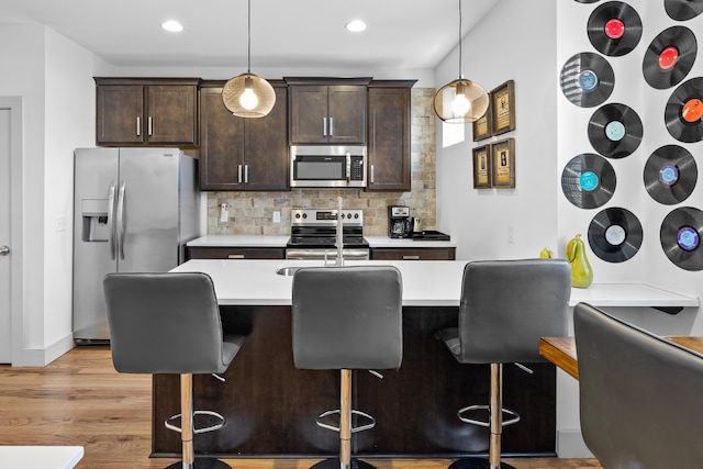 kitchen with a kitchen bar, light hardwood / wood-style flooring, decorative light fixtures, and stainless steel appliances