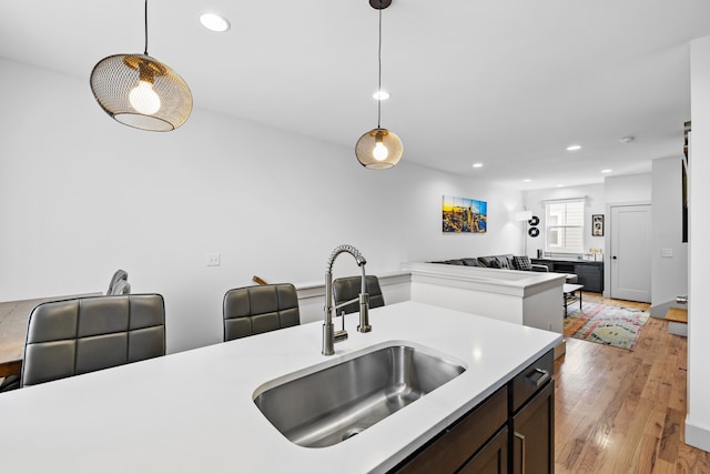 kitchen with sink, light hardwood / wood-style flooring, dark brown cabinetry, and pendant lighting