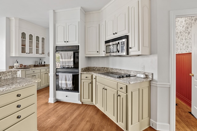 kitchen featuring light wood-type flooring, light stone countertops, cream cabinetry, and black appliances