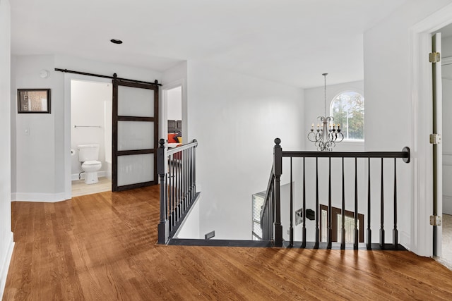 staircase featuring a barn door, an inviting chandelier, and wood-type flooring