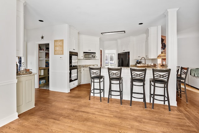 kitchen featuring kitchen peninsula, black refrigerator with ice dispenser, light stone countertops, white cabinets, and light wood-type flooring