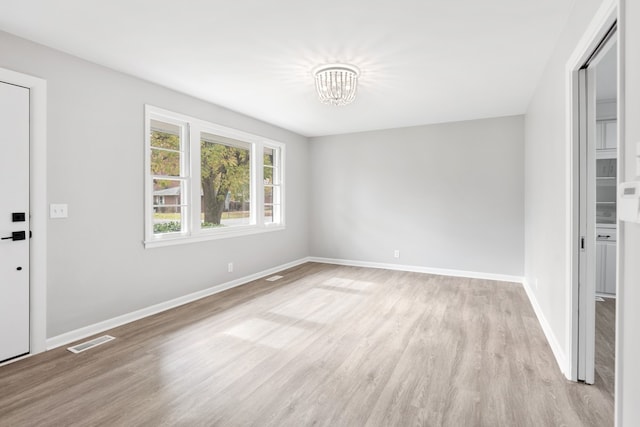 spare room with an inviting chandelier and light wood-type flooring