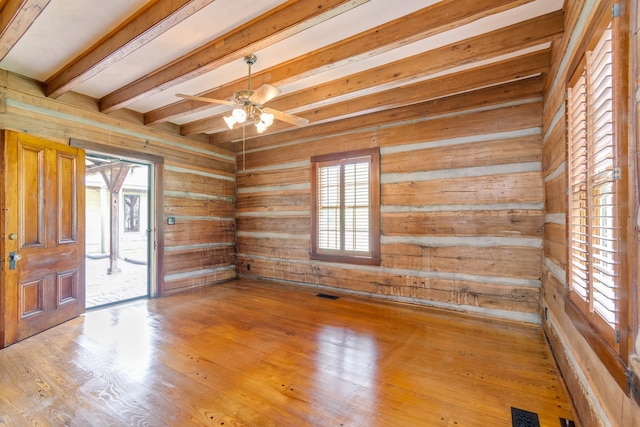 empty room featuring beam ceiling, ceiling fan, light hardwood / wood-style flooring, and wooden walls