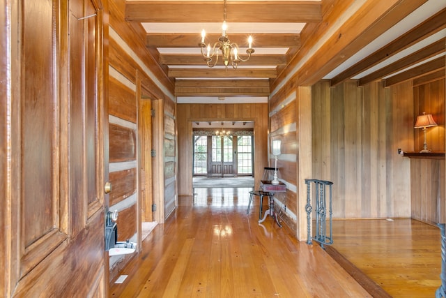 corridor featuring beam ceiling, light wood-type flooring, wooden walls, and a notable chandelier