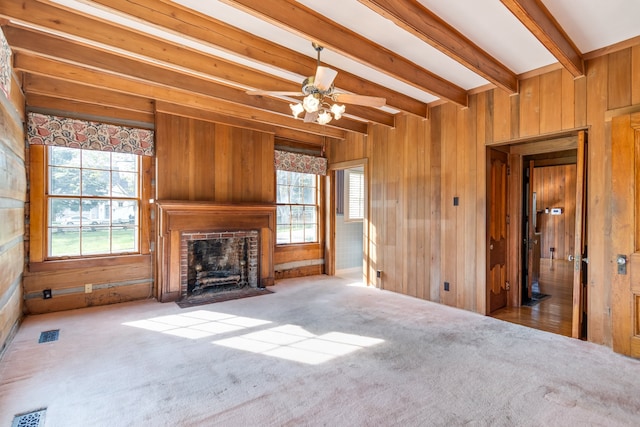 unfurnished living room featuring light carpet, a fireplace, ceiling fan, beamed ceiling, and wood walls