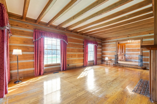 unfurnished living room featuring beamed ceiling, a healthy amount of sunlight, and wood-type flooring