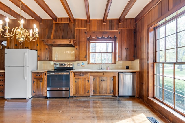 kitchen featuring wooden walls, pendant lighting, stainless steel appliances, and light hardwood / wood-style floors