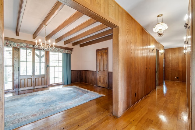 foyer entrance with wood walls, french doors, beam ceiling, a notable chandelier, and light hardwood / wood-style floors