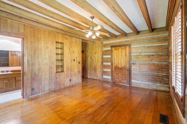 spare room featuring ceiling fan, sink, wood-type flooring, beam ceiling, and wood walls