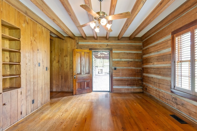 empty room featuring beamed ceiling, a wealth of natural light, and wooden walls