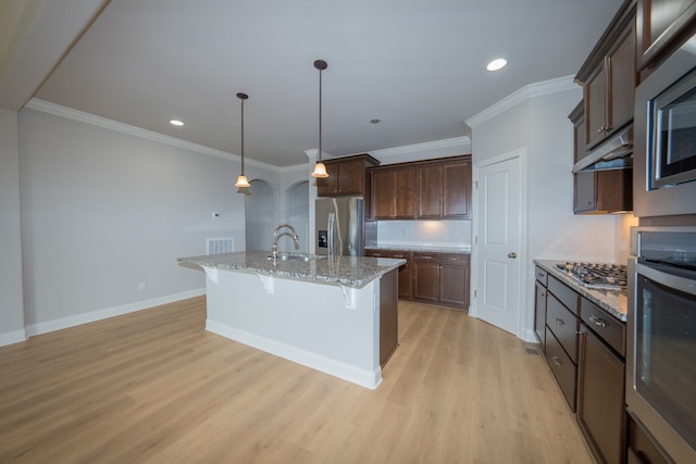 kitchen featuring appliances with stainless steel finishes, an island with sink, a kitchen breakfast bar, light hardwood / wood-style floors, and decorative light fixtures