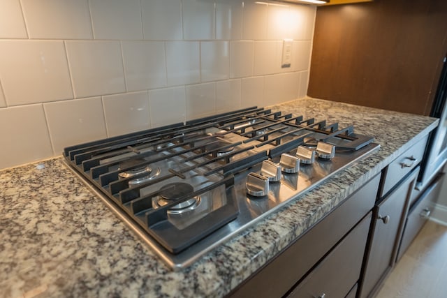 interior details with stainless steel gas stovetop, tasteful backsplash, and dark stone counters