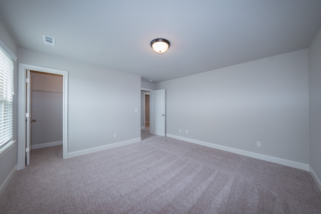 unfurnished bedroom featuring light carpet, a closet, and a walk in closet