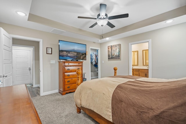 carpeted bedroom with ceiling fan, a raised ceiling, ensuite bathroom, a walk in closet, and a closet