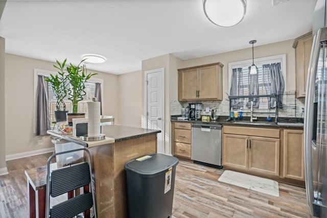 kitchen featuring appliances with stainless steel finishes, light wood-type flooring, tasteful backsplash, sink, and decorative light fixtures