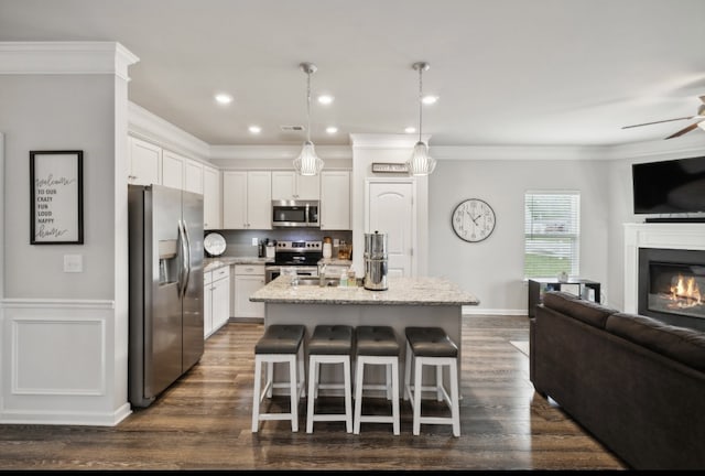 kitchen featuring white cabinets, an island with sink, appliances with stainless steel finishes, light stone countertops, and decorative light fixtures