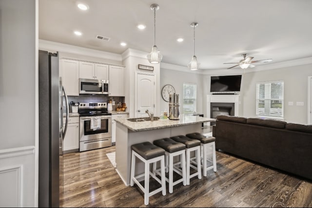 kitchen with white cabinets, stainless steel appliances, light stone countertops, and a kitchen island with sink