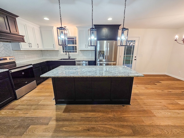 kitchen with a kitchen island, hanging light fixtures, sink, appliances with stainless steel finishes, and light hardwood / wood-style floors