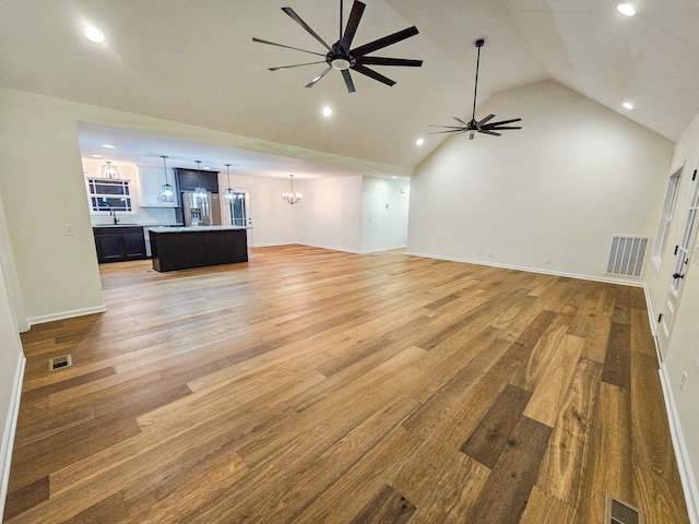 unfurnished living room featuring lofted ceiling, sink, ceiling fan with notable chandelier, and light hardwood / wood-style floors