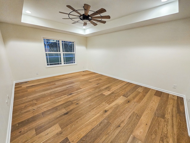 unfurnished room with hardwood / wood-style floors, a tray ceiling, and ceiling fan