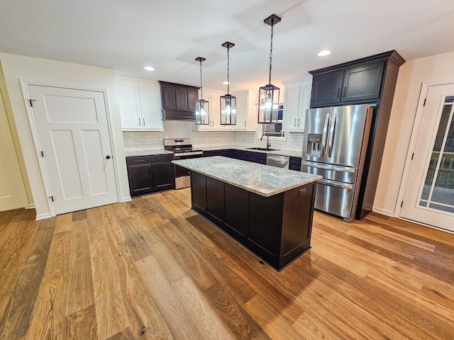 kitchen with decorative backsplash, a kitchen island, light hardwood / wood-style flooring, hanging light fixtures, and appliances with stainless steel finishes