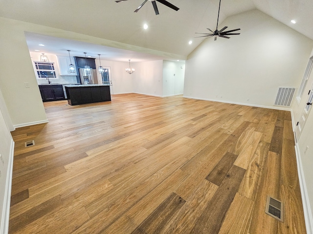 unfurnished living room featuring lofted ceiling, light wood-type flooring, and ceiling fan with notable chandelier