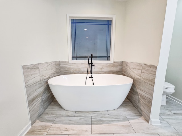 bathroom featuring toilet, a bathing tub, and tile walls