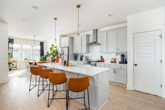 kitchen with a center island with sink, wall chimney exhaust hood, stainless steel appliances, and a breakfast bar area