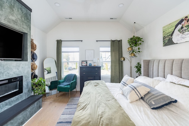 bedroom with hardwood / wood-style flooring, a large fireplace, and lofted ceiling