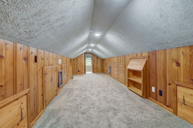 bonus room featuring lofted ceiling, wooden walls, light colored carpet, and a textured ceiling