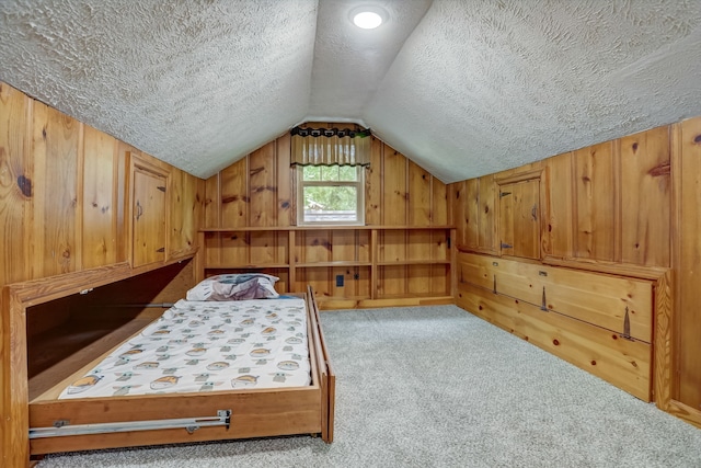 bedroom with lofted ceiling, a textured ceiling, light colored carpet, and wood walls