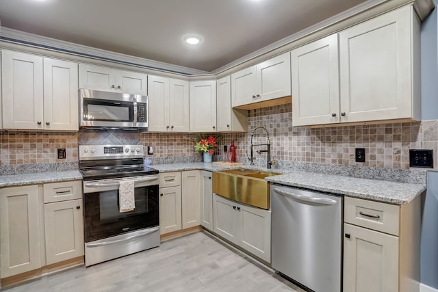 kitchen with backsplash, sink, appliances with stainless steel finishes, light stone counters, and light hardwood / wood-style floors