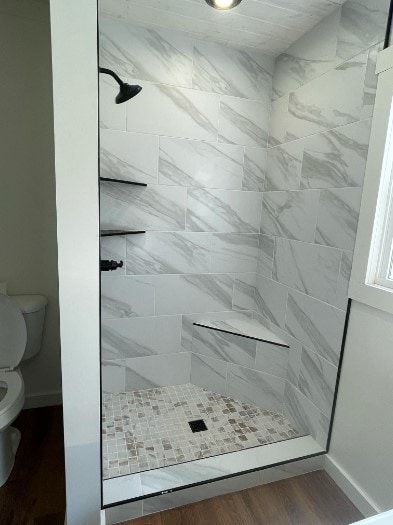 bathroom featuring wood-type flooring, toilet, and tiled shower