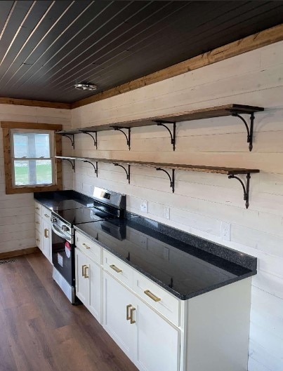 kitchen featuring white cabinetry, dark stone counters, dark hardwood / wood-style floors, stainless steel electric range, and wooden walls