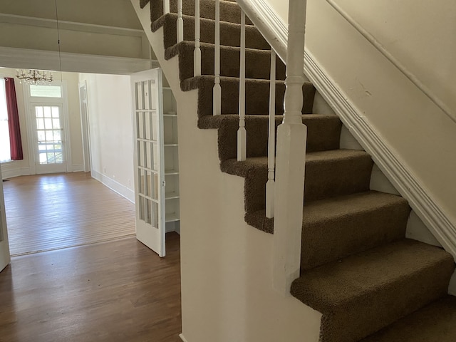 stairs featuring wood-type flooring and an inviting chandelier