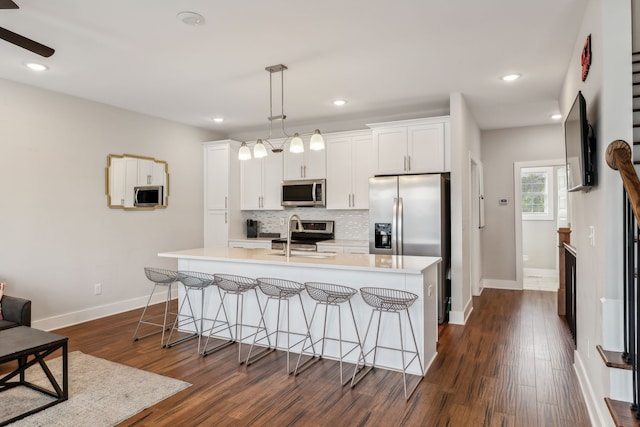 kitchen featuring appliances with stainless steel finishes, pendant lighting, white cabinets, dark wood-type flooring, and a kitchen island with sink