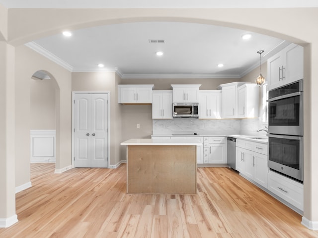 kitchen with hanging light fixtures, a kitchen island, white cabinetry, light wood-type flooring, and stainless steel appliances