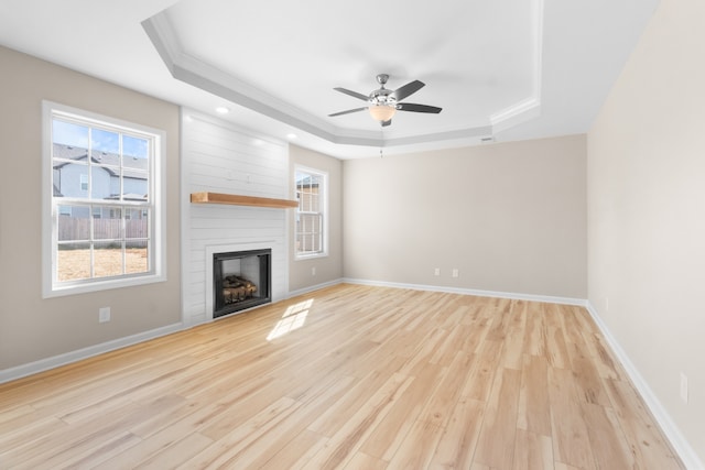 unfurnished living room with light hardwood / wood-style floors, a large fireplace, a tray ceiling, and ceiling fan