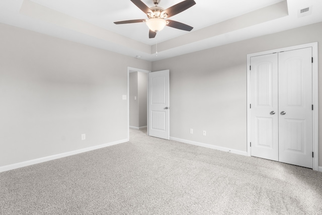 unfurnished bedroom with carpet, a raised ceiling, a closet, and ceiling fan