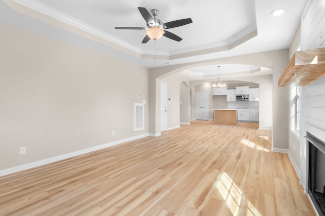 unfurnished living room with crown molding, a tray ceiling, light hardwood / wood-style flooring, and ceiling fan with notable chandelier