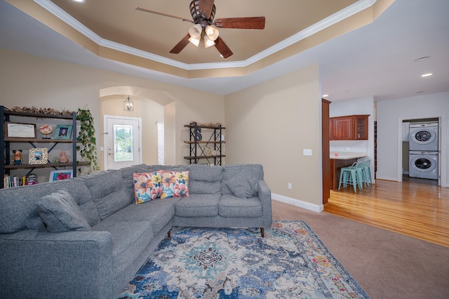 living room with stacked washer / dryer, a raised ceiling, and ornamental molding