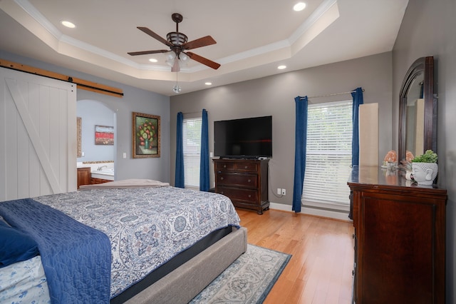 bedroom featuring light hardwood / wood-style flooring, crown molding, a barn door, a raised ceiling, and ceiling fan