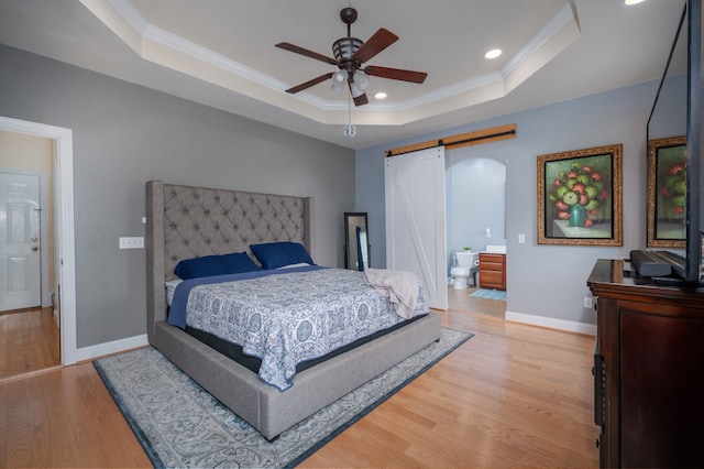 bedroom featuring a raised ceiling, ceiling fan, a barn door, connected bathroom, and light hardwood / wood-style flooring