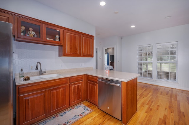 kitchen featuring decorative backsplash, kitchen peninsula, sink, light wood-type flooring, and appliances with stainless steel finishes