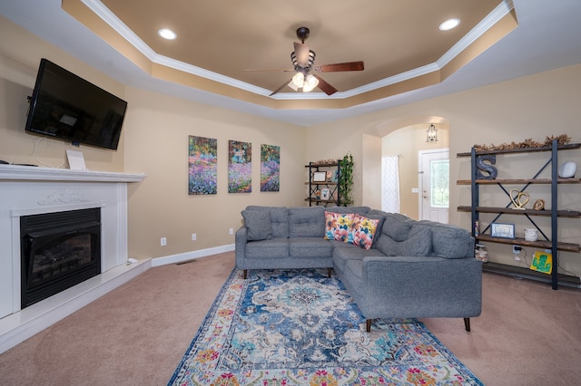 living room with ceiling fan, a tray ceiling, carpet, and ornamental molding