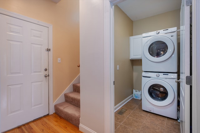 laundry area with light hardwood / wood-style floors, cabinets, and stacked washer and dryer