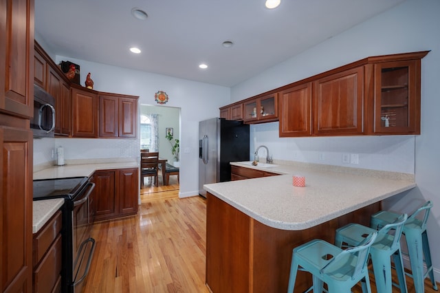 kitchen featuring kitchen peninsula, stainless steel appliances, light wood-type flooring, and a breakfast bar